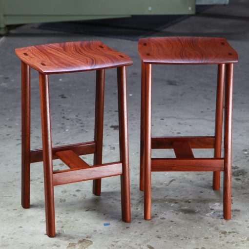 Two perfectly matched jarrah stools sit in a woodworking workshop.