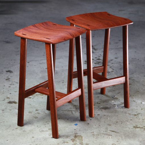 Two perfectly matched jarrah stools sit in a woodworking workshop.