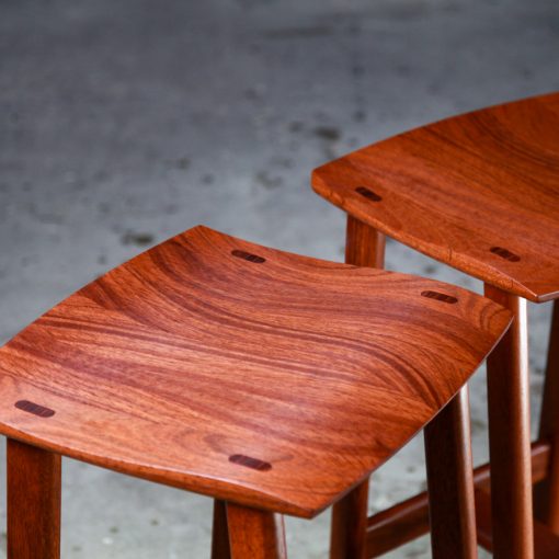 Two perfectly matched jarrah stools sit in a woodworking workshop.