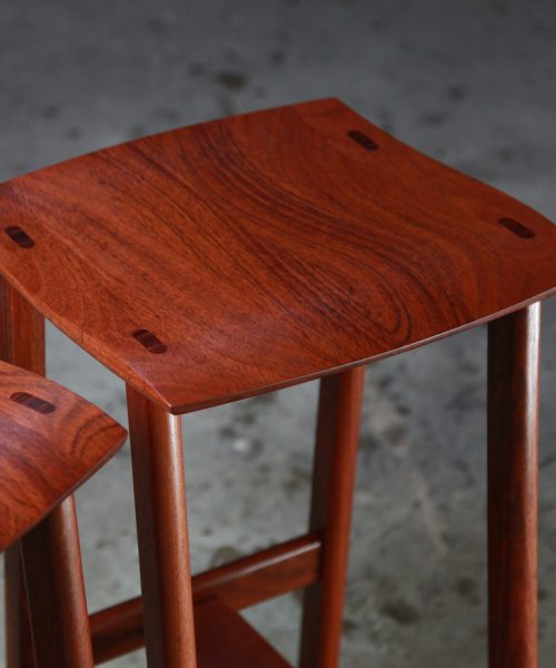 Two perfectly matched jarrah stools sit in a woodworking workshop.