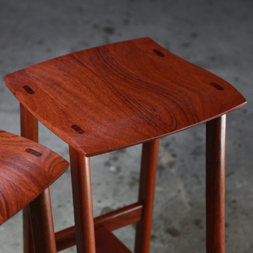 Two perfectly matched jarrah stools sit in a woodworking workshop.