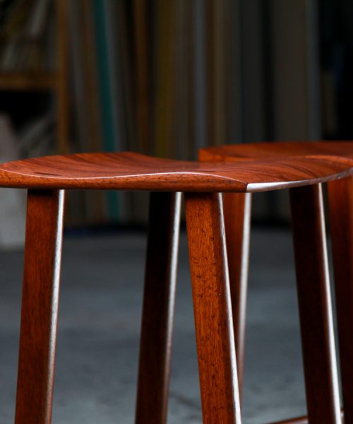 Two perfectly matched jarrah stools sit in a woodworking workshop.