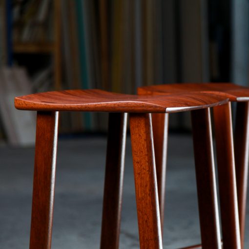 Two perfectly matched jarrah stools sit in a woodworking workshop.