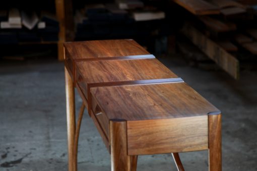 A beautifully composed hall table standing in front of a timber rack in a workshop.