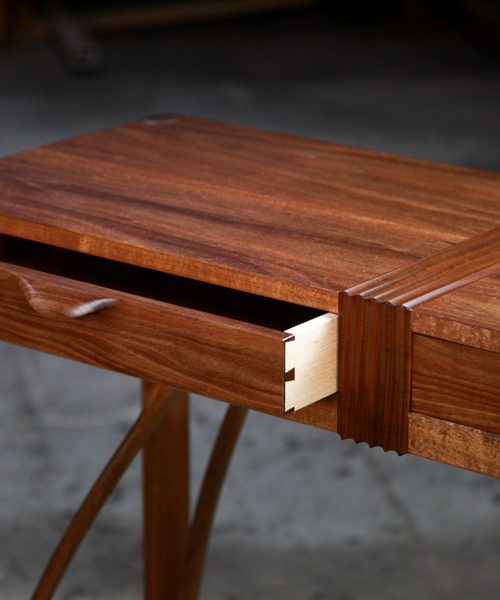 A beautifully composed hall table with figured blackwood standing in front of a timber rack in a woodworking workshop.