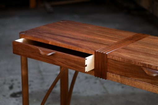 A beautifully composed hall table with figured blackwood standing in front of a timber rack in a woodworking workshop.
