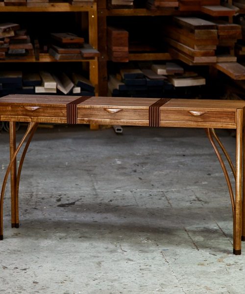 A beautifully composed hall table with figured blackwood standing in front of a timber rack in a woodworking workshop.