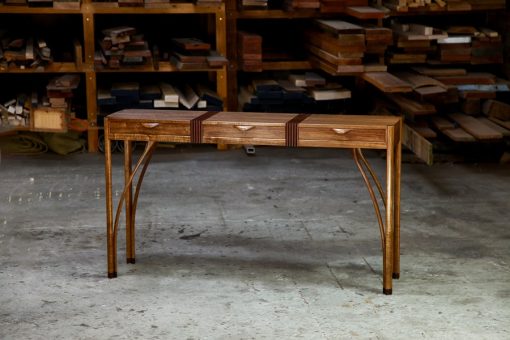 A beautifully composed hall table with figured blackwood standing in front of a timber rack in a woodworking workshop.