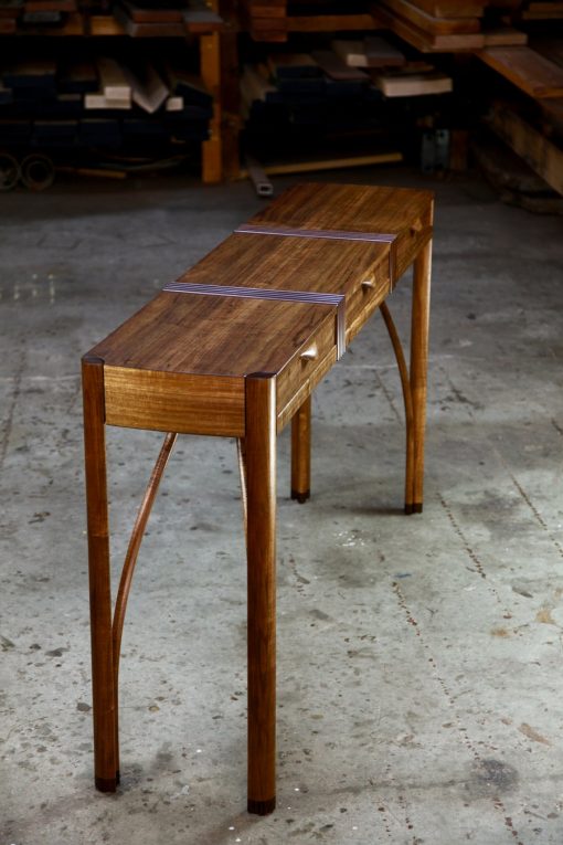 A beautifully composed hall table with figured blackwood standing in front of a timber rack in a woodworking workshop.
