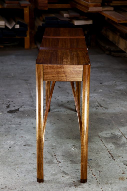 A beautifully composed hall table with figured blackwood standing in front of a timber rack in a woodworking workshop.