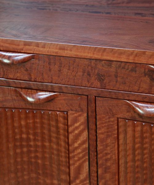 A beautiful red gum cabinet sits in front of a timber rack in a woodworking workshop.