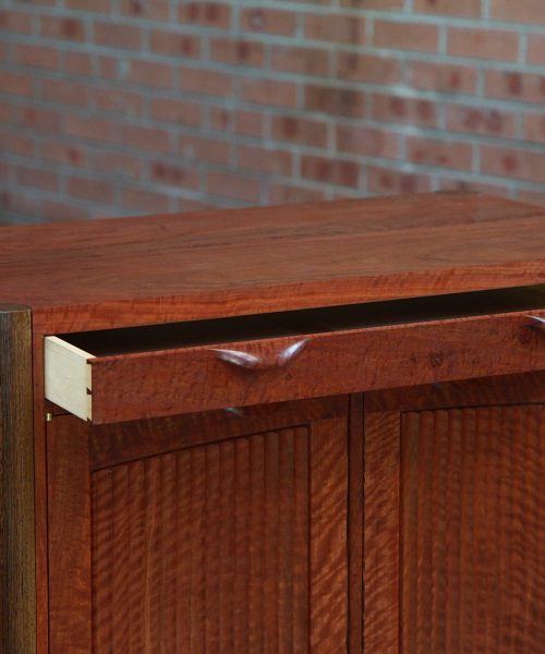 A beautiful red gum cabinet sits in front of a timber rack in a woodworking workshop.
