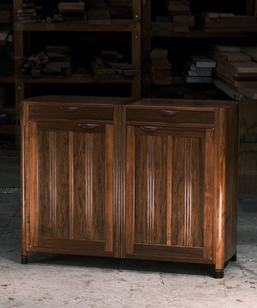 A moody photograph of a blackwood cabinet sits in front of a timber rack in a dark workshop.