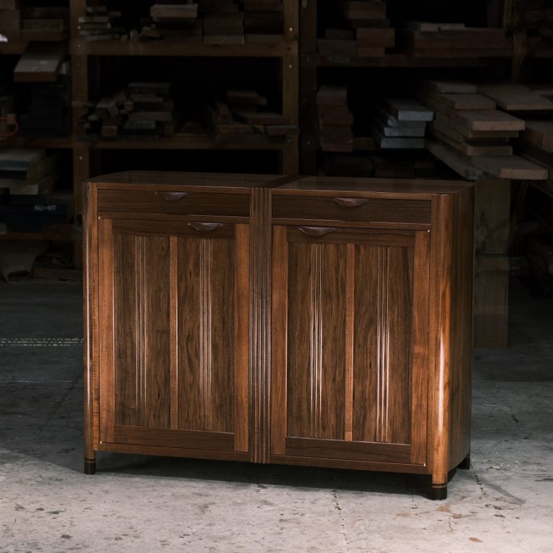 A moody photograph of a blackwood cabinet sits in front of a timber rack in a dark workshop.