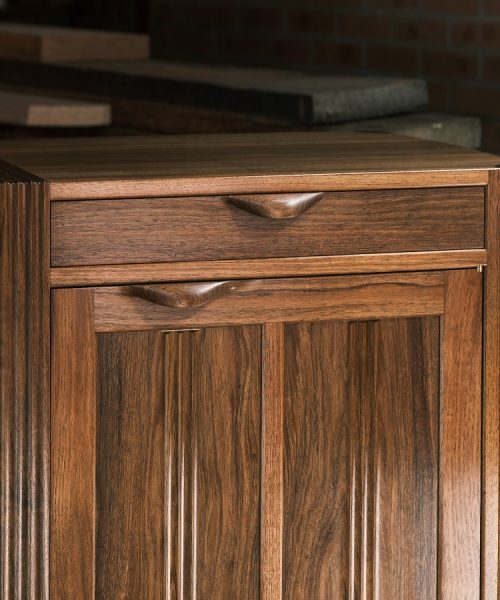 A moody photograph of a blackwood cabinet sits in front of a timber rack in a dark workshop.