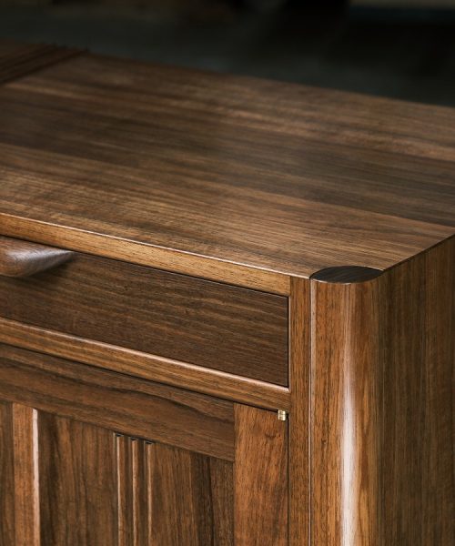 A moody photograph of a blackwood cabinet sits in front of a timber rack in a dark workshop.