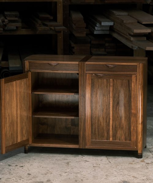 A moody photograph of a blackwood cabinet sits in front of a timber rack in a dark workshop.