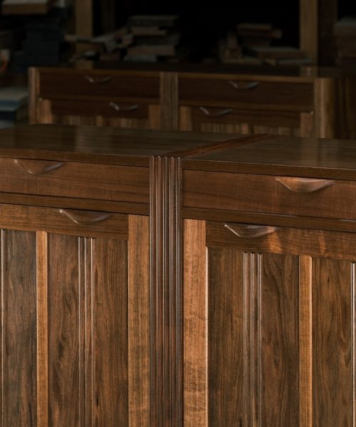 A moody photograph of a blackwood cabinet sits in front of a timber rack in a dark workshop.