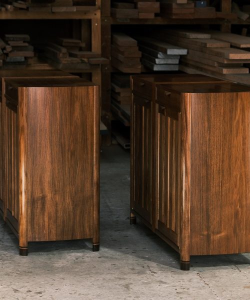 A moody photograph of a blackwood cabinet sits in front of a timber rack in a dark workshop.