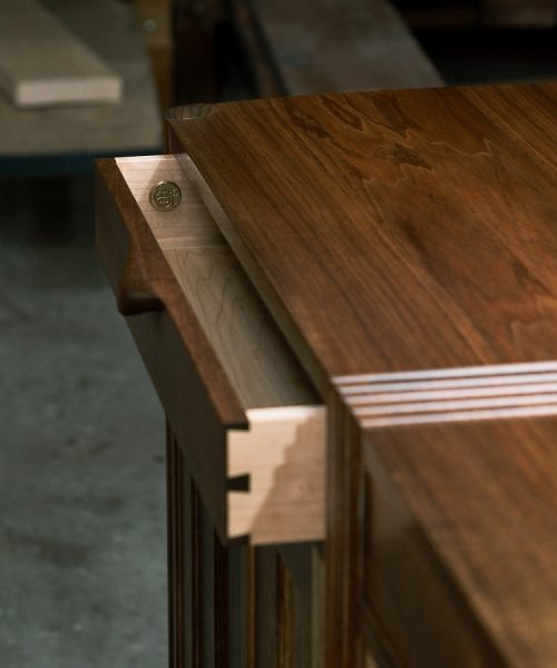 A moody photograph of a blackwood cabinet sits in front of a timber rack in a dark workshop.