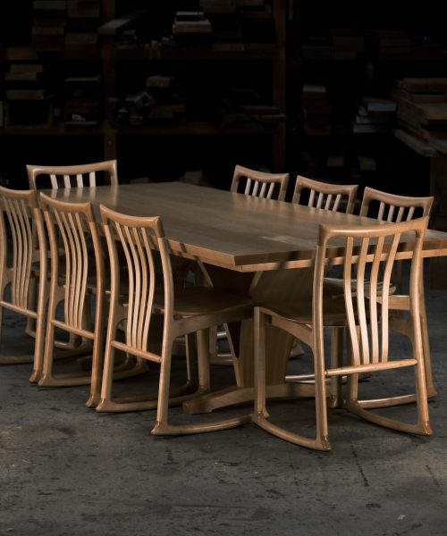 An eight-seater dining suite sitting in a woodworking workshop near a timber rack.