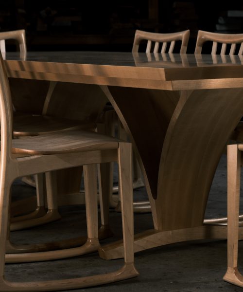 An eight-seater dining suite sitting in a woodworking workshop near a timber rack.