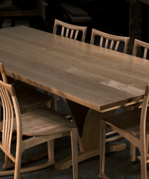 An eight-seater rectangular dining suite sitting in a woodworking workshop near a timber rack.