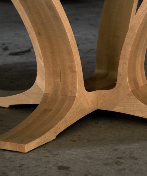 An eight-seater round dining suite sitting in a woodworking workshop near a timber rack.