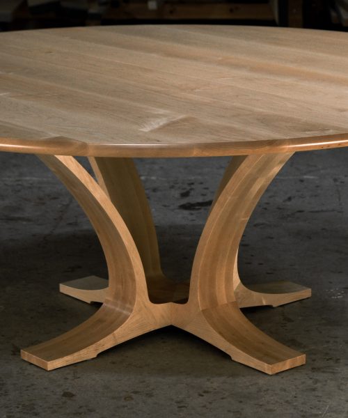 An eight-seater round dining suite sitting in a woodworking workshop near a timber rack.