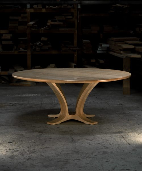 An eight-seater round dining suite sitting in a woodworking workshop near a timber rack.