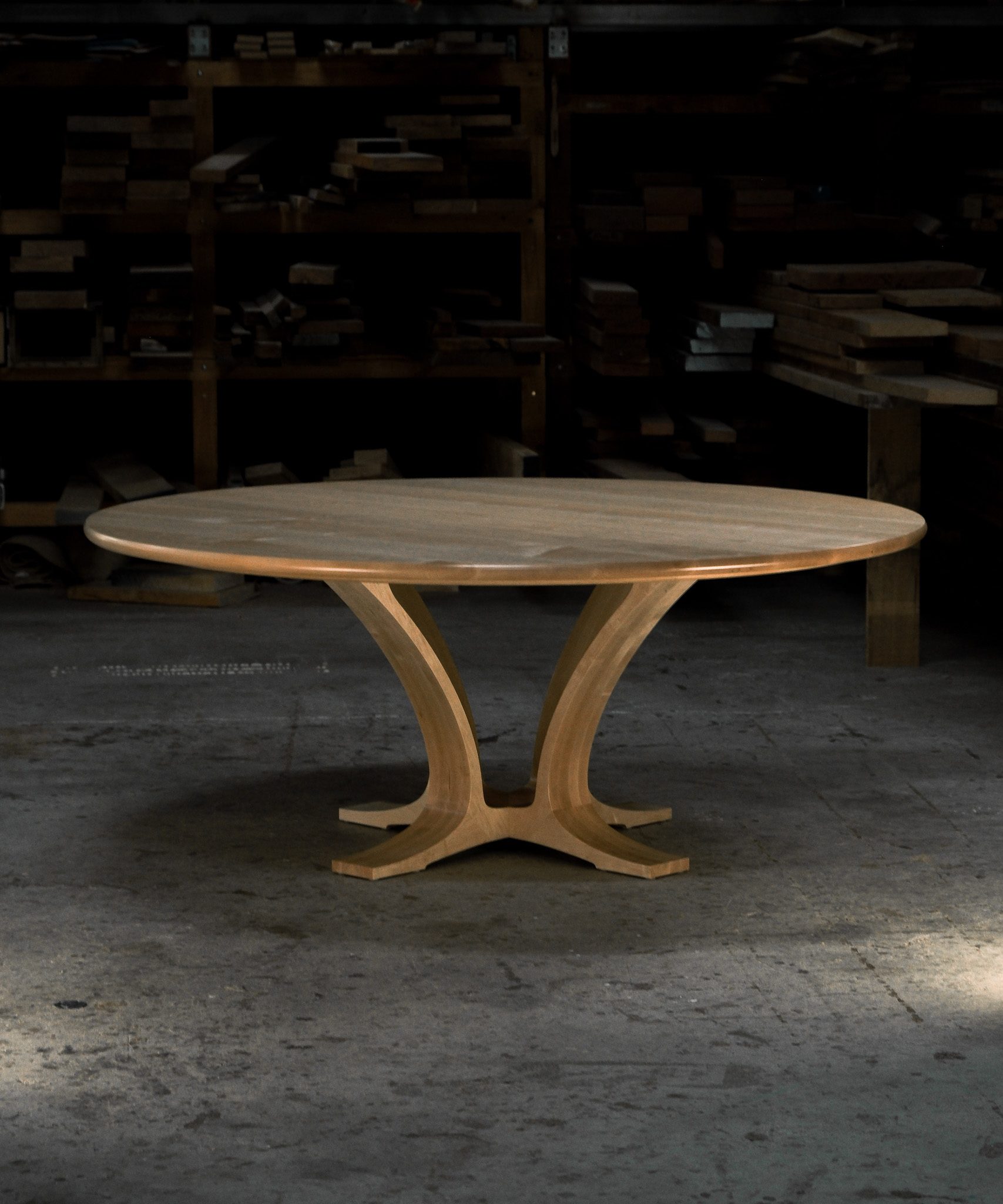 An eight-seater round dining suite sitting in a woodworking workshop near a timber rack.