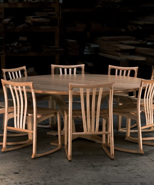 An eight-seater round dining suite sitting in a woodworking workshop near a timber rack.