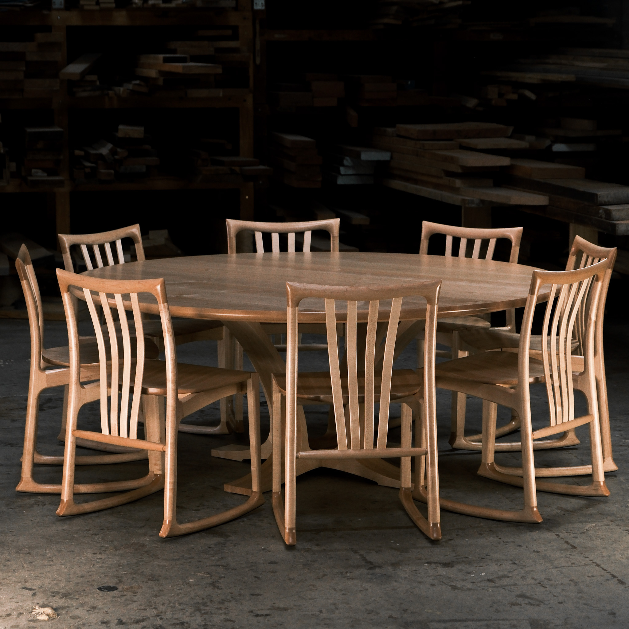 An eight-seater round dining suite sitting in a woodworking workshop near a timber rack.