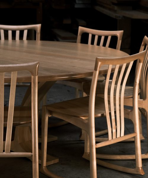 An eight-seater round dining suite sitting in a woodworking workshop near a timber rack.