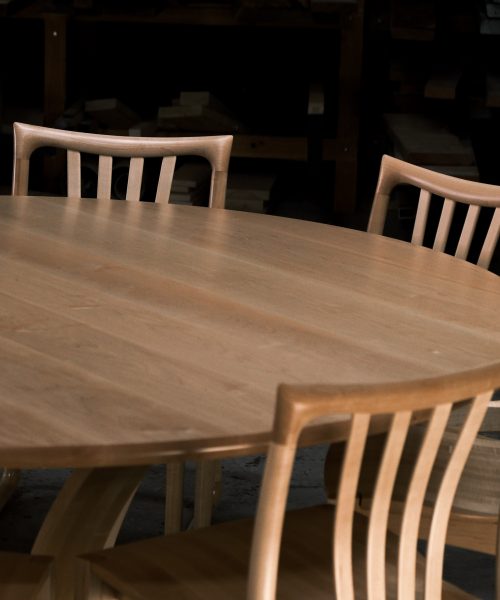 An eight-seater round dining suite sitting in a woodworking workshop near a timber rack.