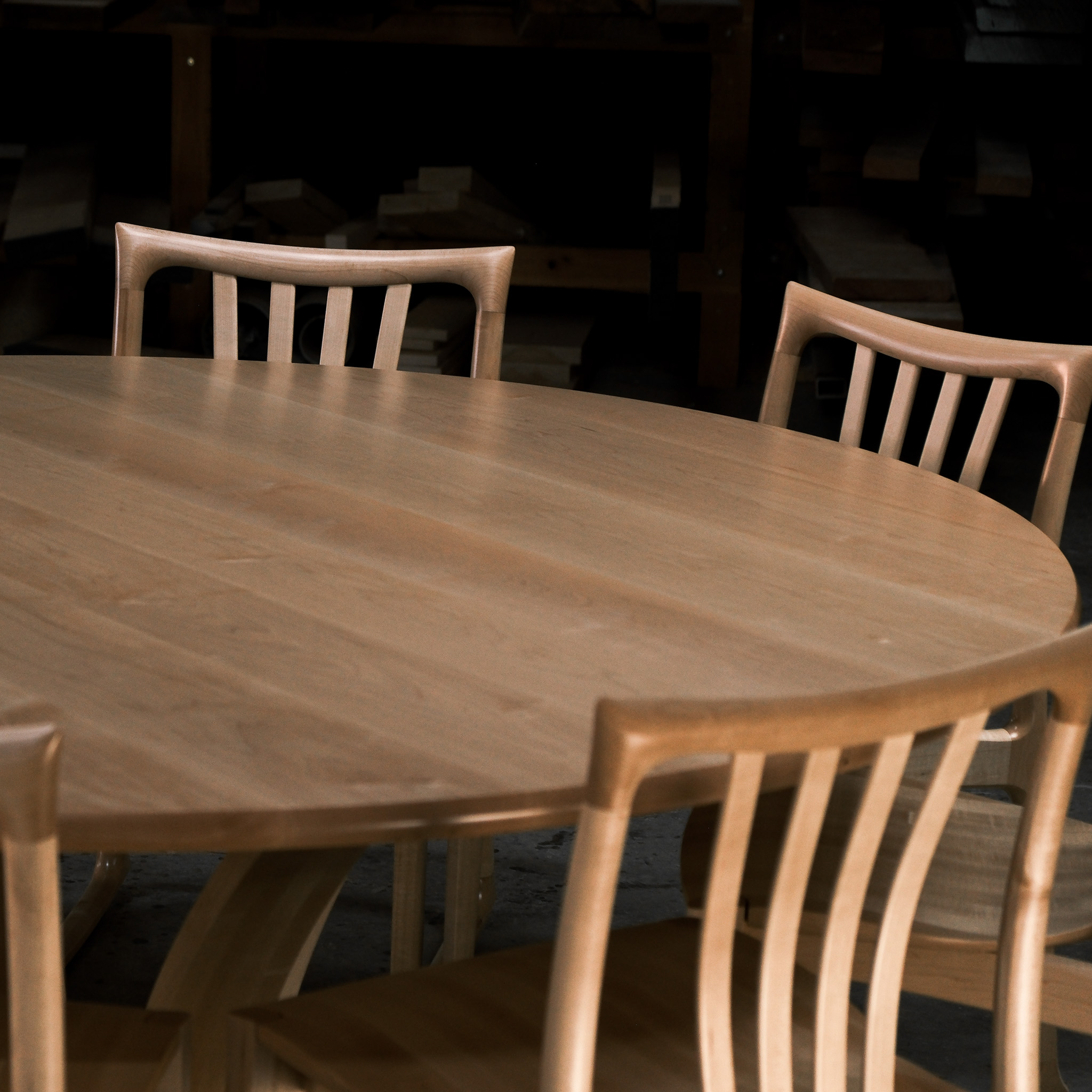 An eight-seater round dining suite sitting in a woodworking workshop near a timber rack.